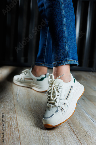 Slender female legs close-up in jeans and white sneakers made of genuine leather.