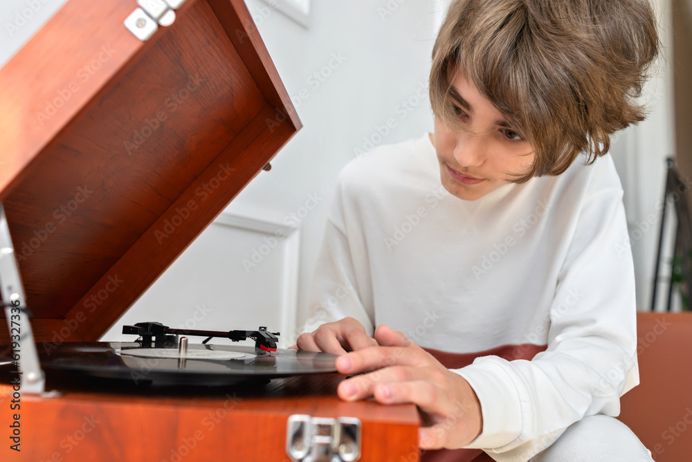 Handsome teenager boy turning on retro vinyl player, brown wooden turntable, listening music, lifestyle