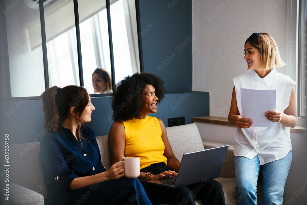 Happy multiracial businesswomensitting on sofa discussing in creative office