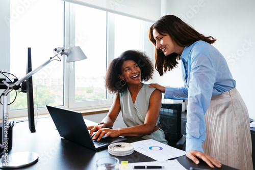 Smiling businesswoman discussing with colleague over laptop at desk in office photo