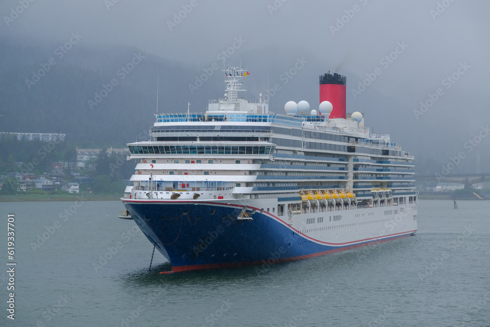 Modern cruiseship cruise ship liner Luminiosa anchored in Juneau bay, Alaska during heavy rain and low cloud nature scenery with mountains and foggy misty atmosphere	