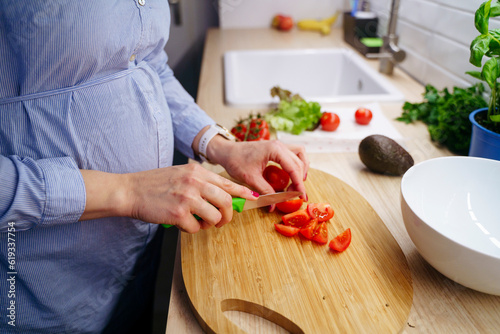 Pregnant woman cutting tomatoes with knife at home photo
