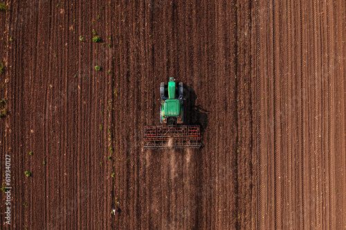 Green tractor vehicle with tiller attached performing field tillage before the sowing season, aerial shot seen from the drone pov photo