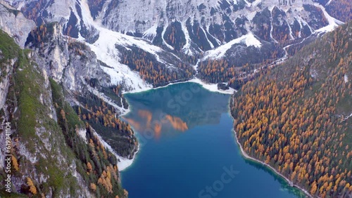 4K aerial - a bird's eye view video (Ultra High Definition) of Braies Lake with recreational boats. Aerial autumn scene from flying drone of Dolomite Alps, Italy. Beauty of nature concept background.