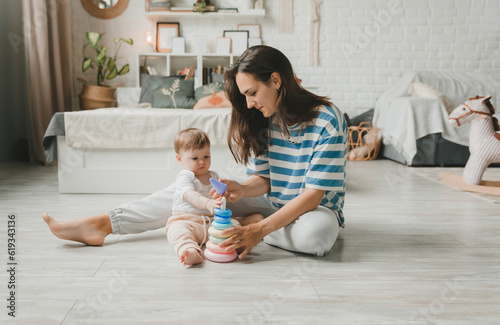Beautiful young mother plays and teaches her baby 6 months old on the floor in the living room.mom and baby play with toys