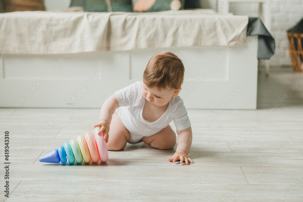 baby 6-9 months old playing with a colorful rainbow toy pyramid sitting in a white sunny bedroom. Toys for small children. Children's interior. A child with an educational toy. baby 6-9 months old playing with a colorful rainbow toy pyramid sitting in a white sunny bedroom. Toys for small children. Children's interior. A child with an educational toy.