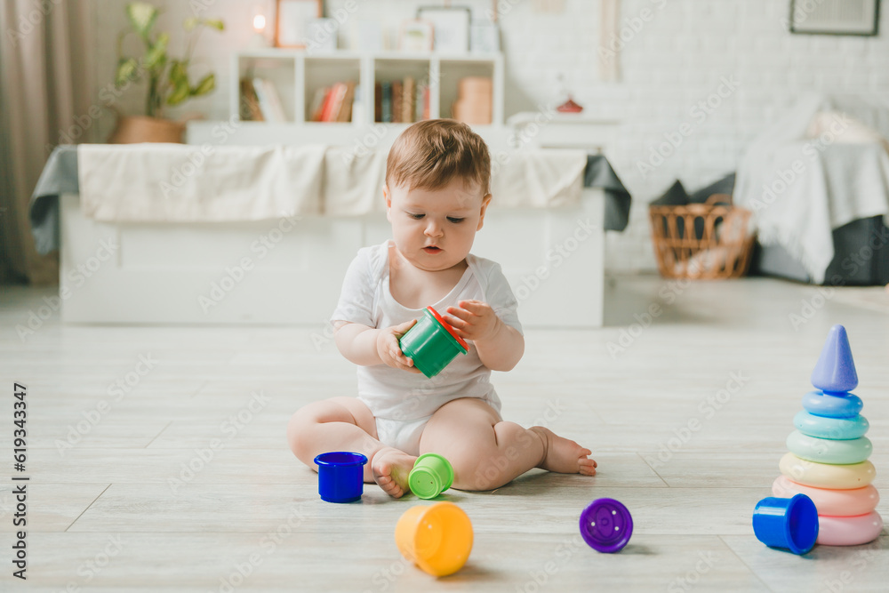 baby 6-9 months old playing with a colorful rainbow toy pyramid sitting in a white sunny bedroom. Toys for small children. Children's interior. A child with an educational toy. baby 6-9 months old playing with a colorful rainbow toy pyramid sitting in a white sunny bedroom. Toys for small children. Children's interior. A child with an educational toy.