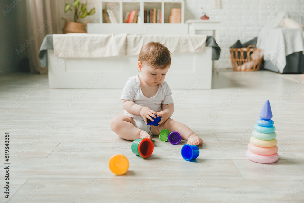 baby 6-9 months old playing with a colorful rainbow toy pyramid sitting in a white sunny bedroom. Toys for small children. Children's interior. A child with an educational toy. baby 6-9 months old playing with a colorful rainbow toy pyramid sitting in a white sunny bedroom. Toys for small children. Children's interior. A child with an educational toy.