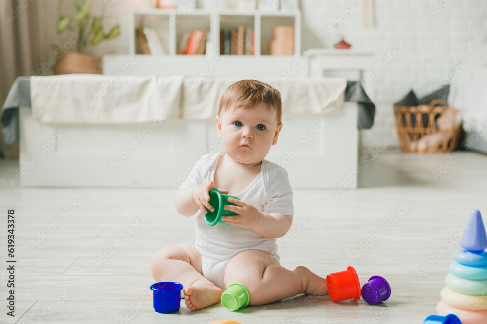baby 6-9 months old playing with a colorful rainbow toy pyramid sitting in a white sunny bedroom. Toys for small children. Children's interior. A child with an educational toy. baby 6-9 months old playing with a colorful rainbow toy pyramid sitting in a white sunny bedroom. Toys for small children. Children's interior. A child with an educational toy.