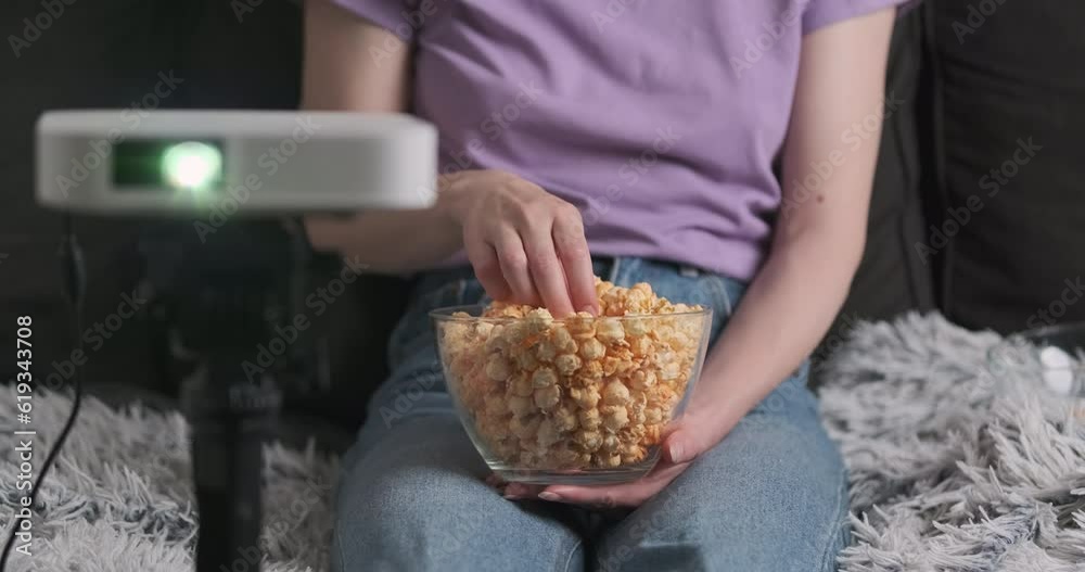 Woman's hands eat popcorn, girl watches movie on home projector. Unrecognizable, front view. Woman's hands eat popcorn, girl watches movie on home projector. Unrecognizable, front view.
