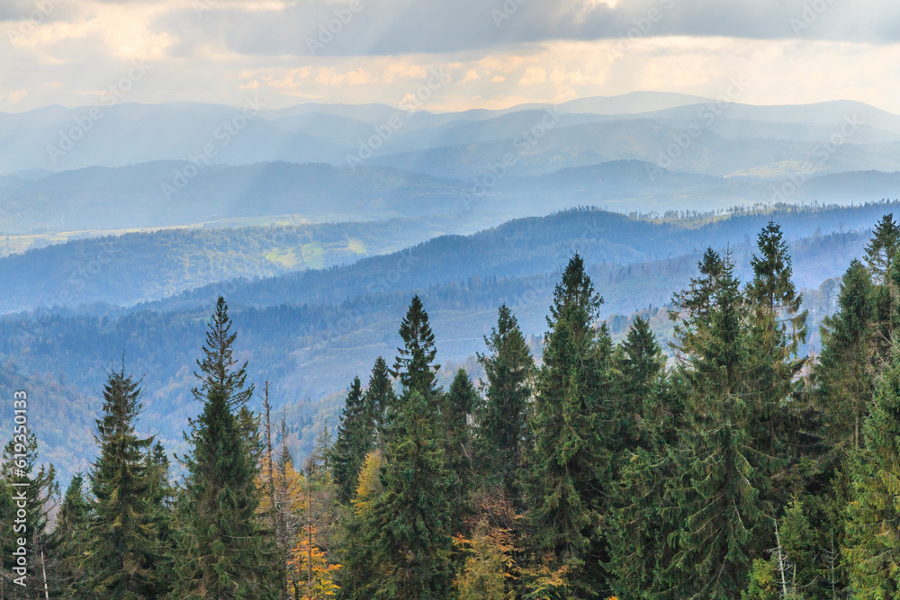 Autumn view of the peaks of Beskid Żywiecki from the tourist trail to Magurka Radziechowska near Żywiec (Poland) with a cloudy sky with streaks of sun