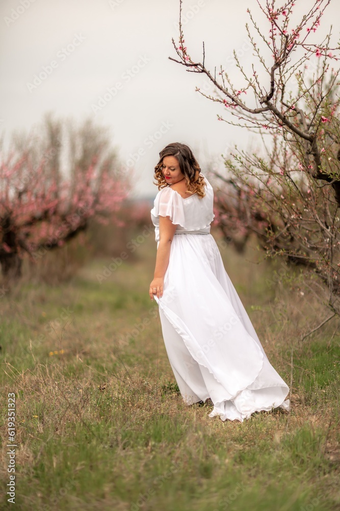 Woman peach blossom. Happy woman in white dress walking in the garden of blossoming peach trees in spring