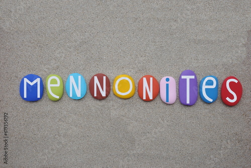 Mennonites, groups of Anabaptist Christian church communities of denominations, creative text composed with multi colored stone letters over beach sand