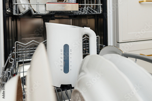 A close-up of a modern white dishwasher with a kettle inside, showing the economical design and technology used to clean dishes in domestic households.