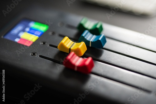 Daytime photo of a grey music studio desk with music production setup and colorful faders. 