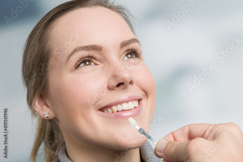 Close up of dentist using shade guide at woman s mouth to check veneer of teeth for bleaching 