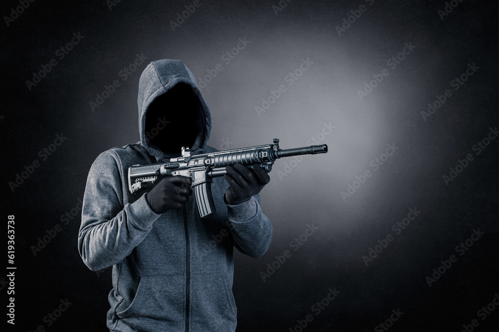 Hooded man with assault rifle over dark misty background Hooded man with assault rifle over dark misty background