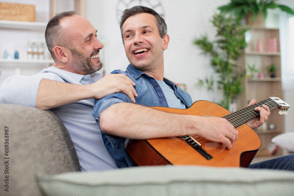 Fototapeta premium gay couple with guitar sitting on sofa at home