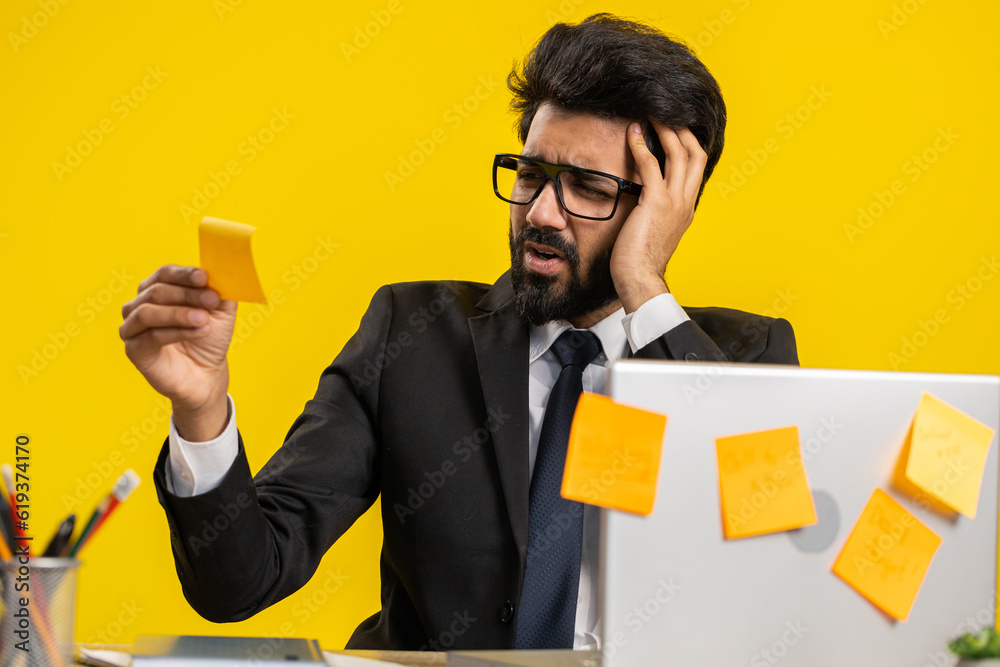 Tired exhausted indian businessman working on laptop at office with many sticker task inscriptions. Freelancer man busy occupation feels sad boredom overworked multitasking. Panic attack, deadline Tired exhausted indian businessman working on laptop at office with many sticker task inscriptions. Freelancer man busy occupation feels sad boredom overworked multitasking. Panic attack, deadline