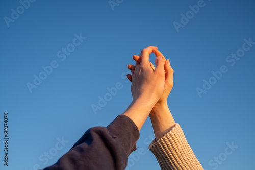 Two persons holding hands against blue sky at sunset