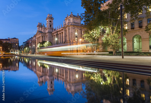 Budapest Parliament Square with Fountain water, moving tram and reflection. Museum of Ethnography in background. Moving effect because of longer exposure.