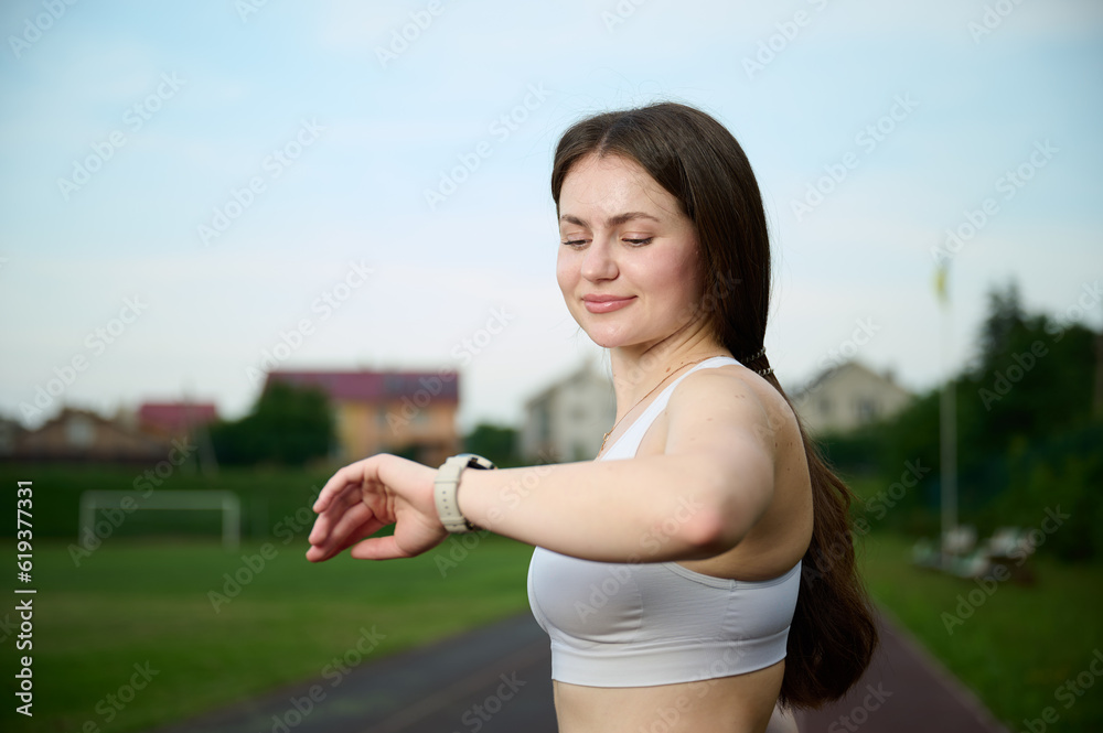 Close up portrait of active attractive beautiful strong female with smartwatch on hand monitoring heart rate after running. Caucasian female jogger runner running on jogging track. Sport and health. Close up portrait of active attractive beautiful strong female with smartwatch on hand monitoring heart rate after running. Caucasian female jogger runner running on jogging track. Sport and health.