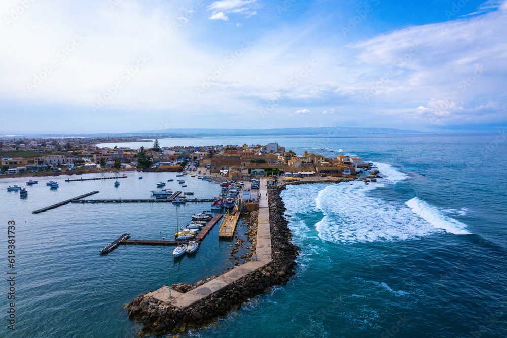 Aerial shot of a small harbor with blue ocean waves crashing into the small Italian town.
