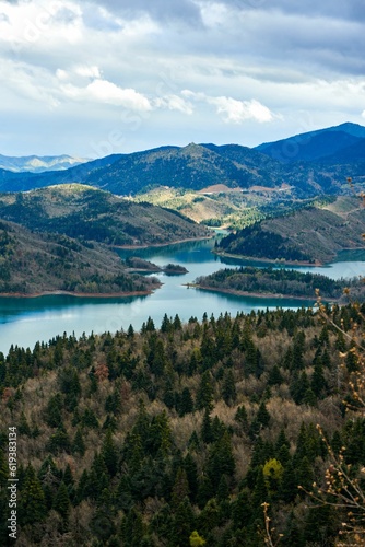 A lake surrounded by wooded trees on a mountain slope with cloudy skies