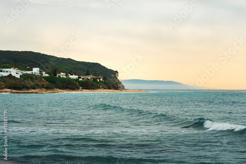 Scenic view of the calm sea with a green hill in the background. Los Canos de Meca, Spain.