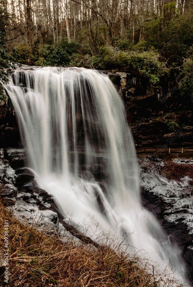 Obraz premium Long exposure shot of a majestic waterfall cascading into a lush grassy field.
