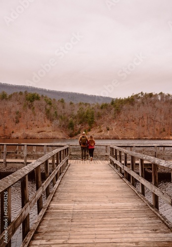 Young man and woman walk across a picturesque wooden bridge over a tranquil lake.