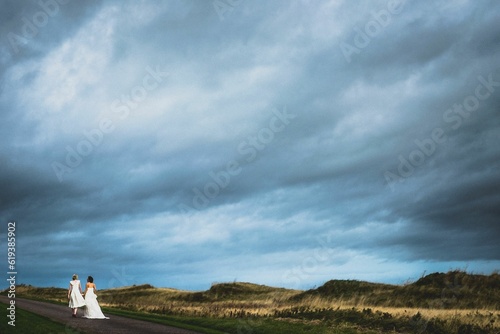 LGBTQ newly weds walking on a road in a green field on a cloudy day