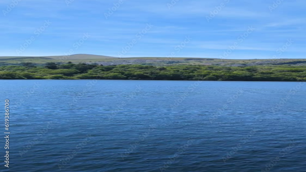 View of blue lake with green coast hills with blue sky by a side walk with green fence View of blue lake with green coast hills with blue sky by a side walk with green fence