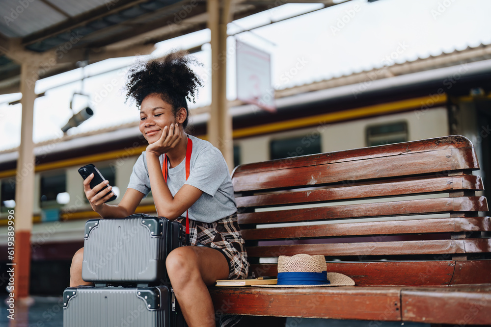 Fototapeta premium Asian teenage girl african american traveling using smartphone moblie while waiting for a train at a station.