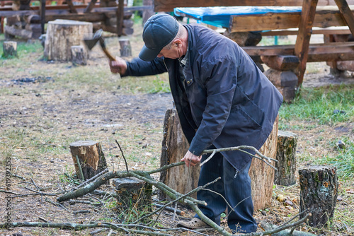 Elderly retired man chopping firewood with an ax, cooking grilled food on a fire
