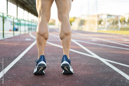 Photo of muscular legs of an unrecognizable athlete posing on an outdoor running track on tiptoe. Concept of running, exercise on an athletics track. Copyspace. photo