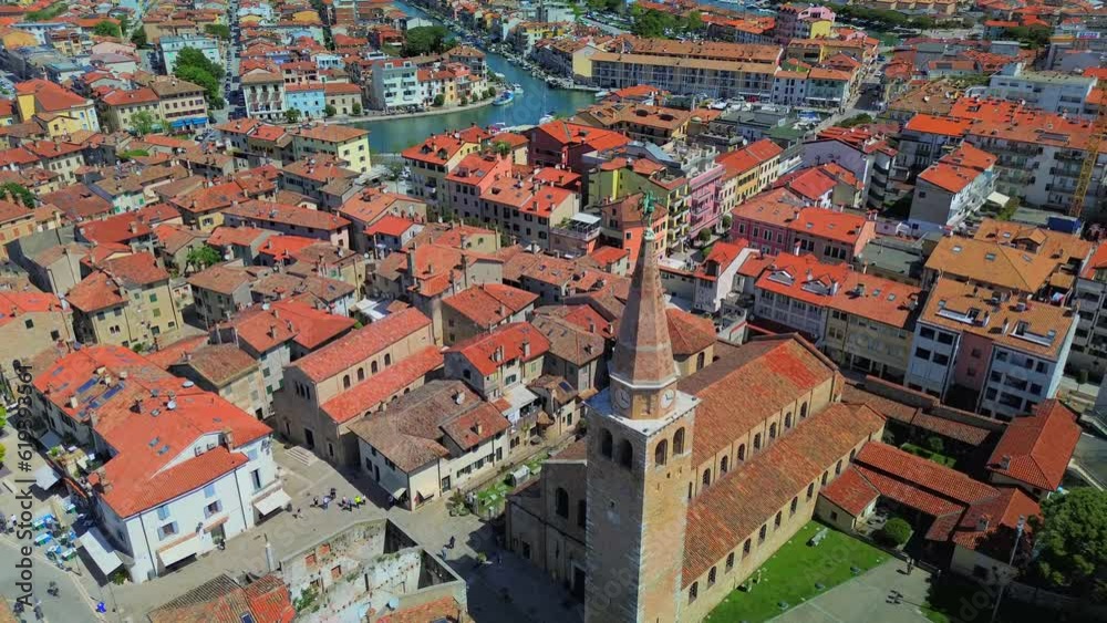 Aerial view of the old city. Roofs of buildings with red tiles and many chimneys. The bell tower of the Catholic Cathedral in the city center. Traveling through narrow streets. Italy Grado 07.2023