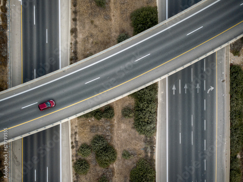 A top down view from a drone of a red car driving on an interchange 