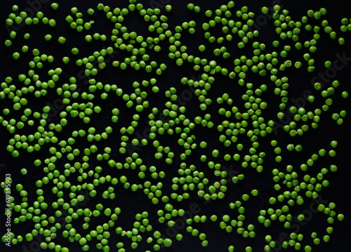 Seeds of green young peas are randomly scattered on a black background.