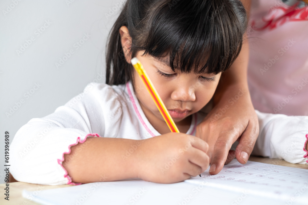 Asian girls aged 4-5 are having mom help with homework, kids holding pencils and writing homework. Asian girls aged 4-5 are having mom help with homework, kids holding pencils and writing homework.