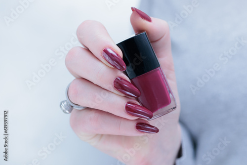 Woman hand with long nails and a bottle of dark red burgundy nail polish photo