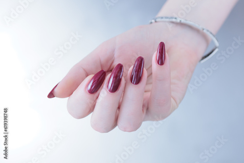 Woman hand with long nails and a bottle of dark red burgundy nail polish photo