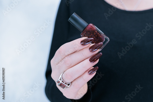 Woman hand with long nails and a bottle of dark red burgundy nail polish photo