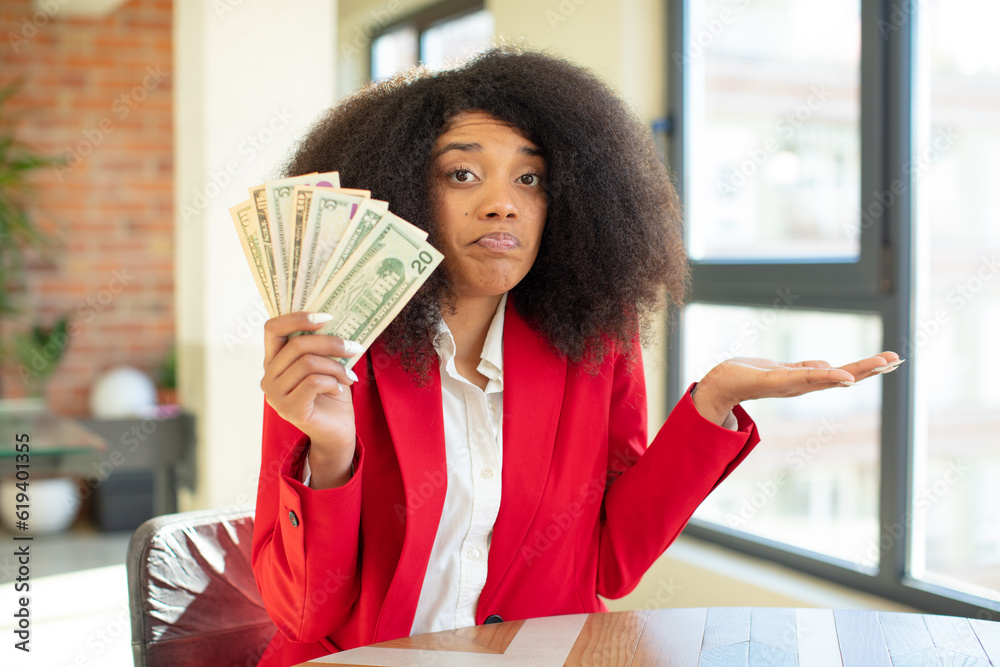 pretty afro black woman shrugging, feeling confused and uncertain. dollar banknotes concept pretty afro black woman shrugging, feeling confused and uncertain. dollar banknotes concept