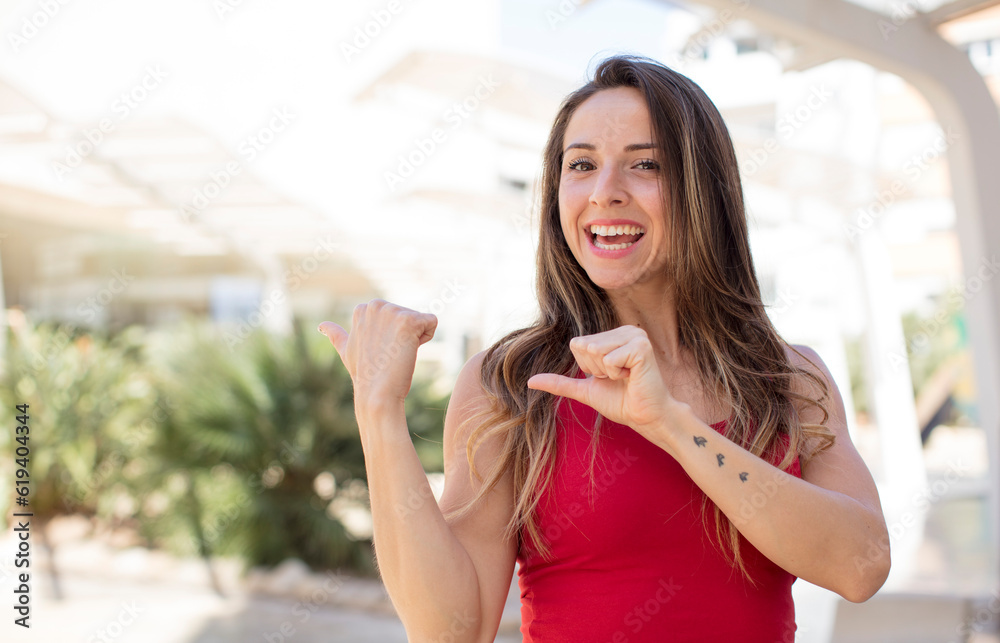 pretty woman smiling cheerfully and casually pointing to copy space on the side, feeling happy and satisfied