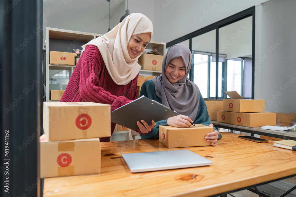 Muslim two woman freelancer sme business online shopping working on laptop computer and checklist order box at home Business online shipping and delivery concept Muslim two woman freelancer sme business online shopping working on laptop computer and checklist order box at home Business online shipping and delivery concept