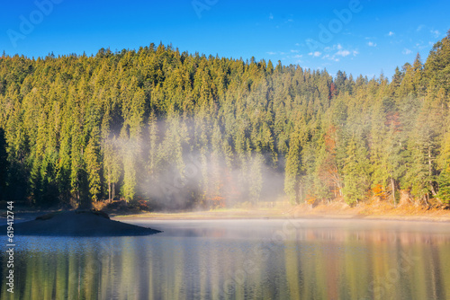 sunny landscape with lake in autumn. fog above the water surface. sky and trees reflection