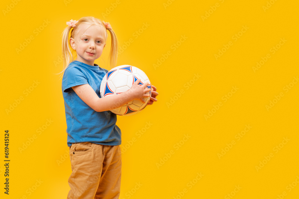 Studio shot of young blonde girl holding soccer ball against yellow background. Child and football. Copy space, mockup Studio shot of young blonde girl holding soccer ball against yellow background. Child and football. Copy space, mockup