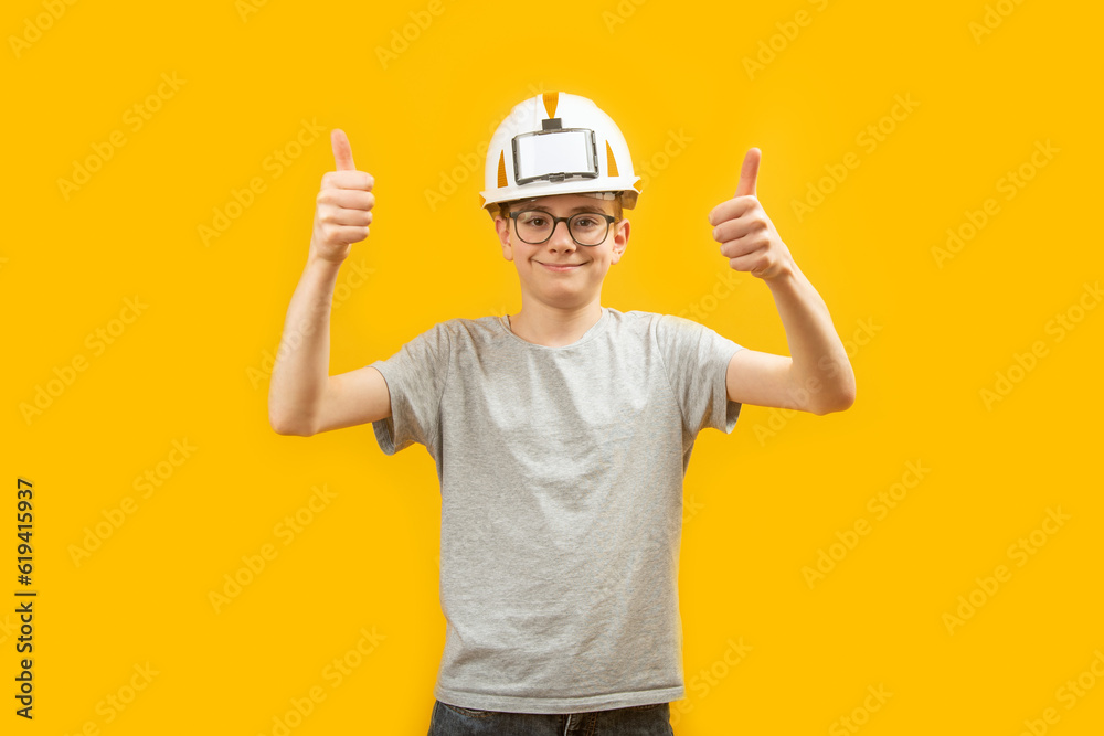 Teenage high school student wears protective helmet and shows thumbs up with two hands on yellow background. Choice of profession.