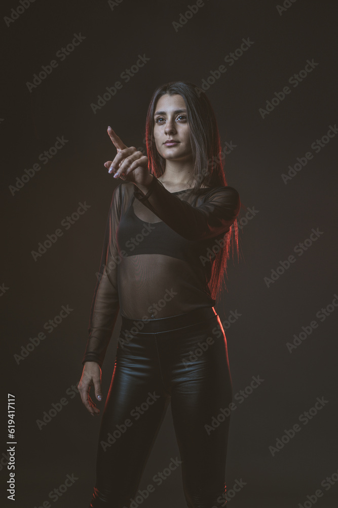 Portrait of beautiful cyber model woman posing wearing black leather leggings outfit with neon glow fluorescent led light in a black background typing in the air Portrait of beautiful cyber model woman posing wearing black leather leggings outfit with neon glow fluorescent led light in a black background typing in the air